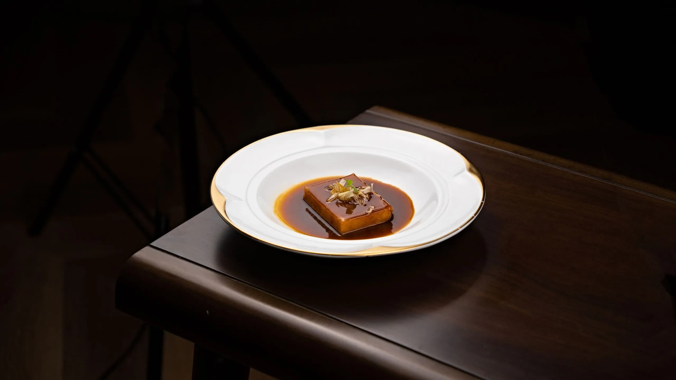 Une assiette dressée, nappée d'une sauce sombre, seule sur une table en bois dans la pénombre