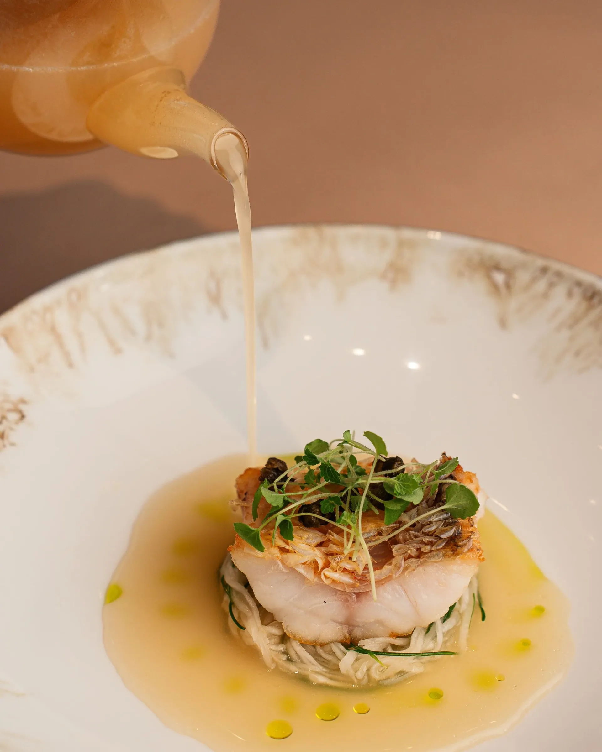 Un bouillon versé sur un poisson aux herbes, dans une assiette creuse