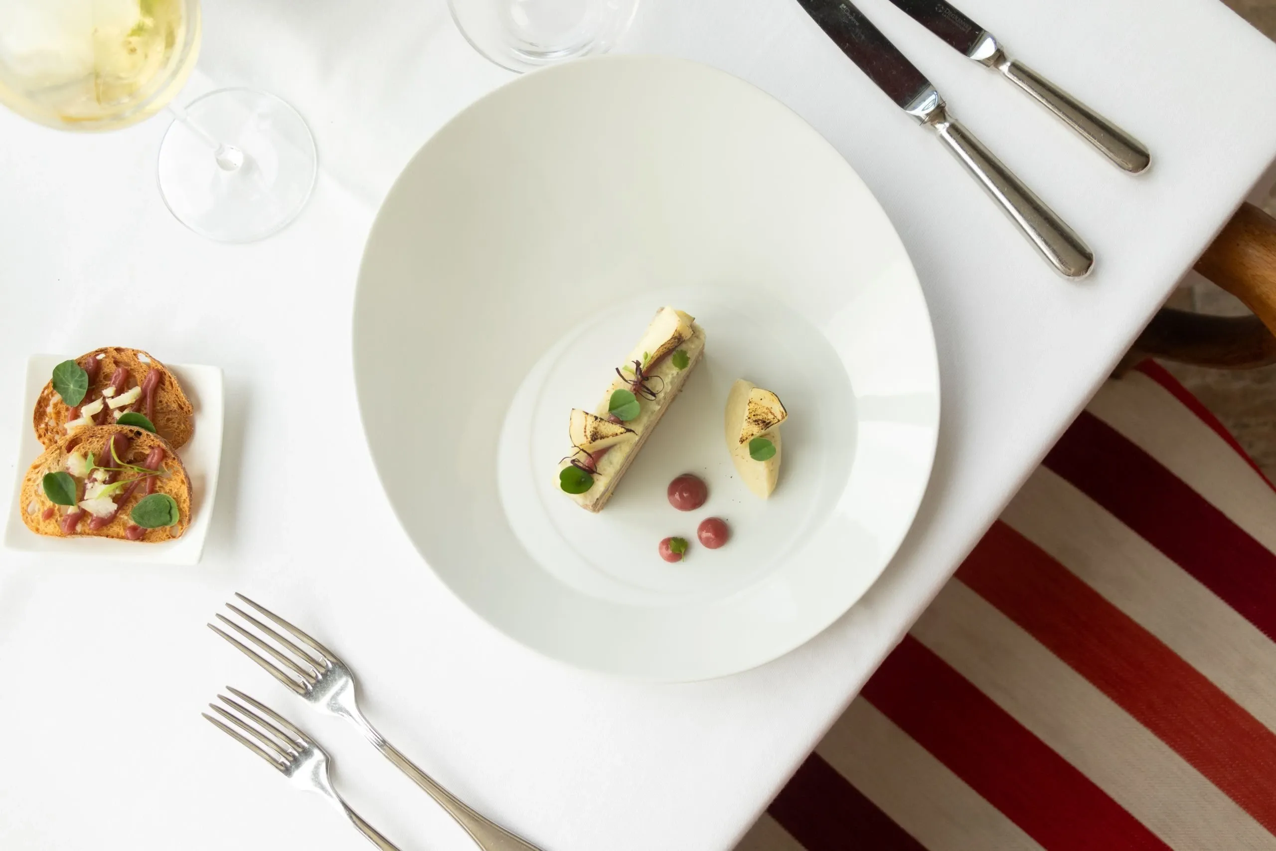 Vue du dessus d'une table nappée de blanc : assiette, couverts, verres et bouchées